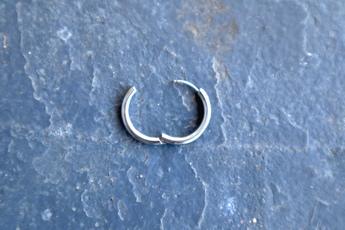 A steel hoop earring opened slightly, resting against a blue surface