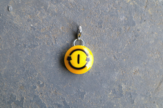 a yellow billiard ball pendant marked "1" with 2 black stars on both sides of the number. A silver clasp is attached to the top of the pendant against a blue/gray surface