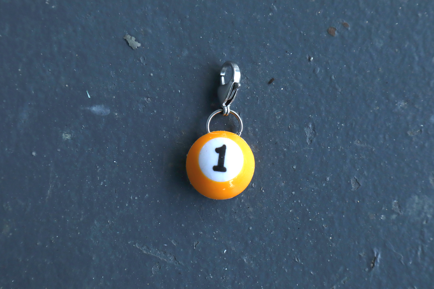 Small yellow billiard ball charm with number 1 on a dark blue background