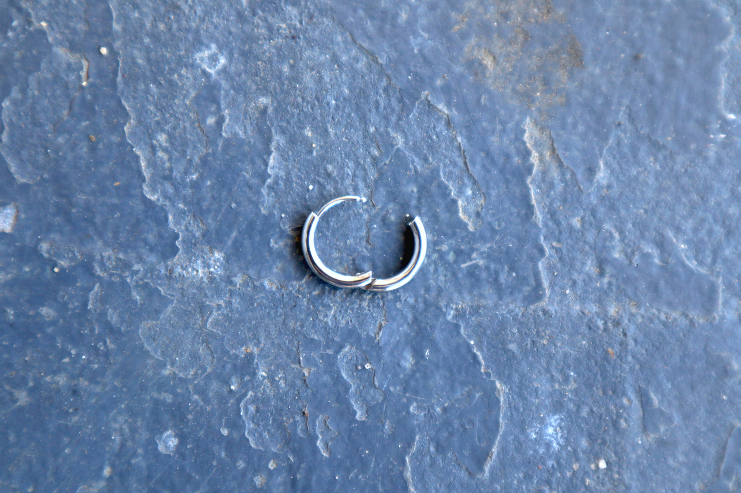 A steel hoop earring opened slightly, resting against a blue surface