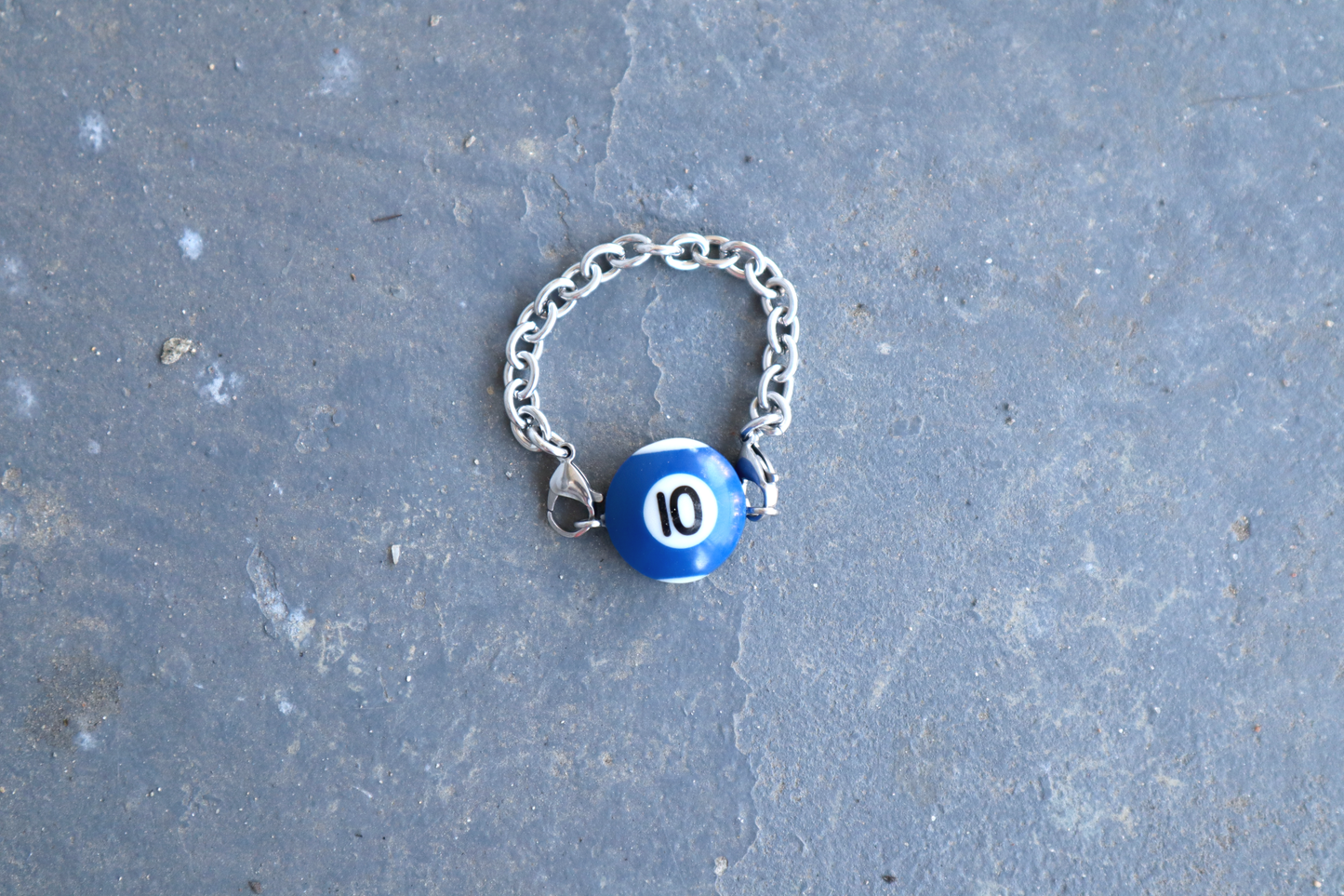 Silver chain bracelet with a blue and white billiard ball pendant marked "10" on a blue/gray surface.