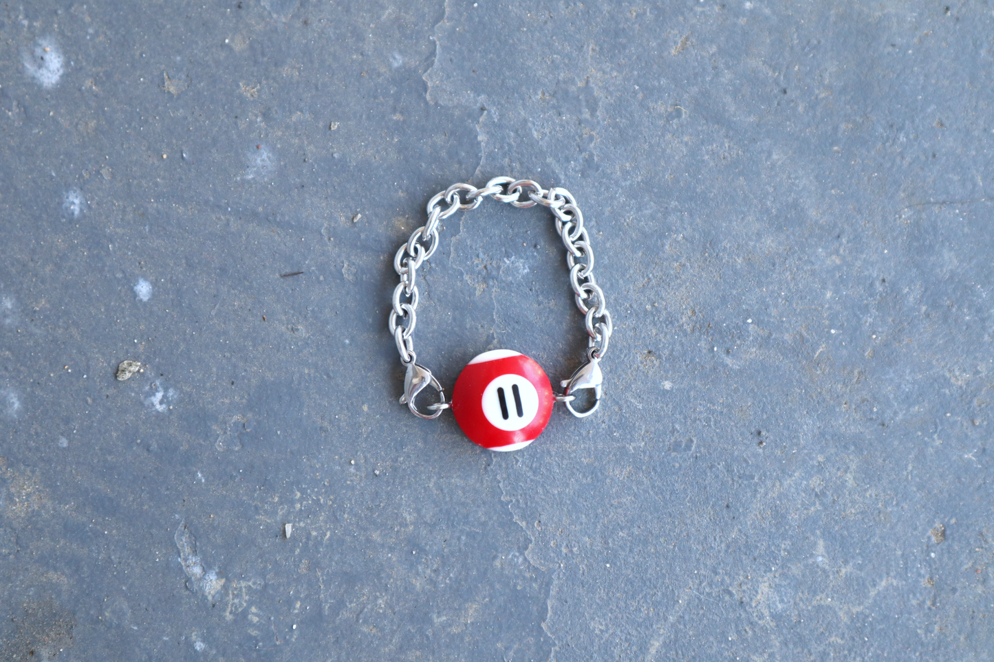Silver chain bracelet with a red and white billiard ball pendant marked "11" on a blue/gray surface.