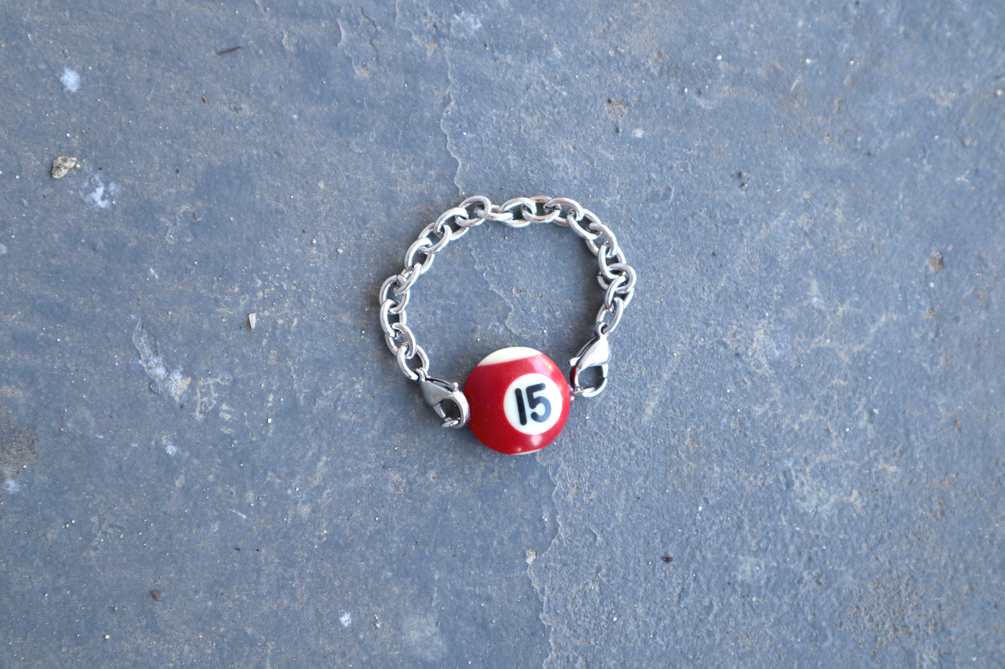 Silver chain bracelet with a red and white billiard ball pendant marked "15" on a blue/gray surface.