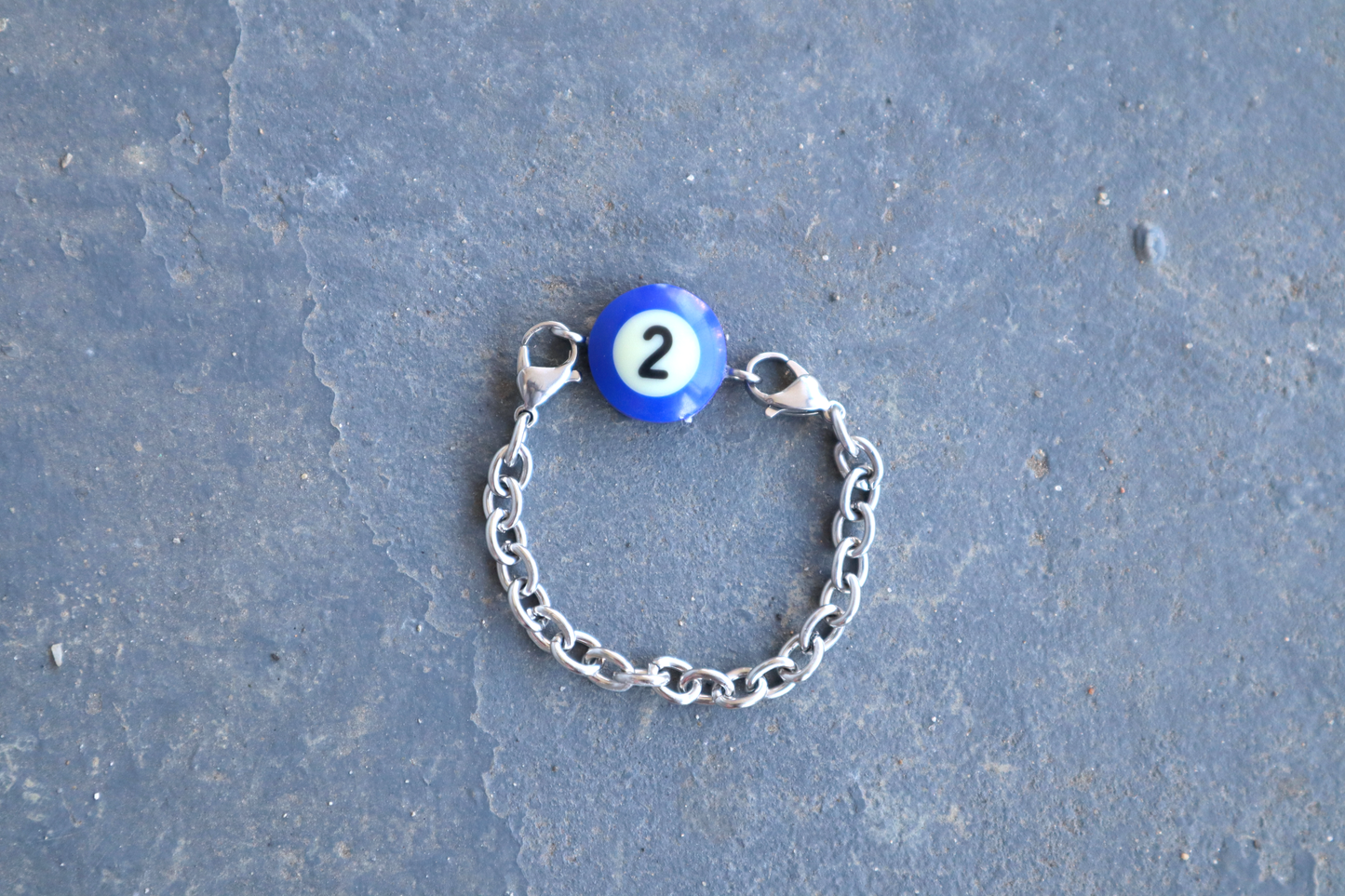 Silver chain bracelet with a blue billiard ball pendant marked "2" on a blue/gray surface.