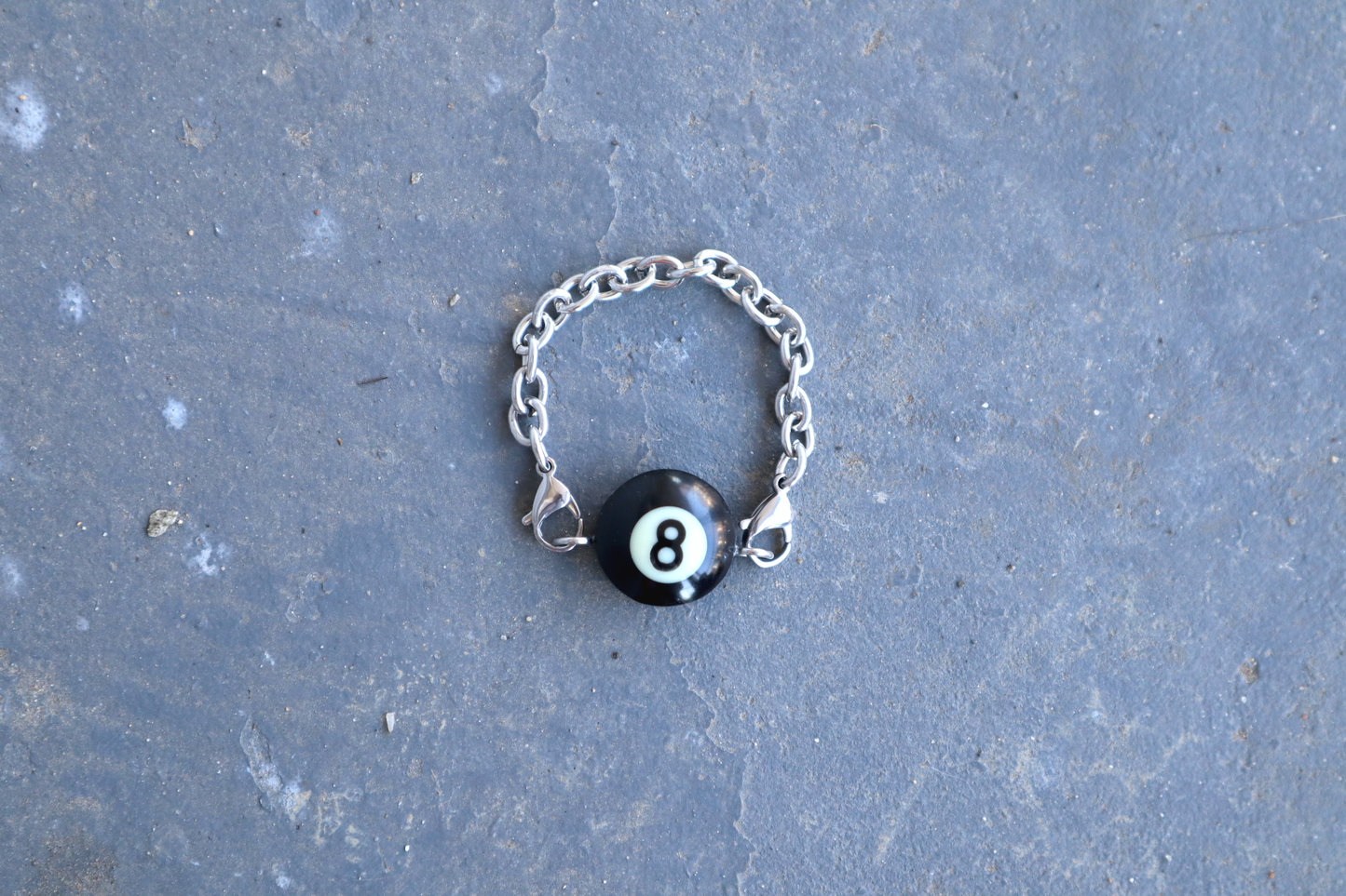 Silver chain bracelet with a black billiard ball pendant marked "8" on a blue/gray surface.