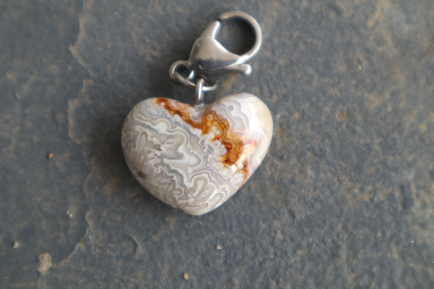 heart-shaped white pendant with gray, yellow and red stick-like patterns. A silver clasp is attached to the top of the pendant, resting on a gray surface.