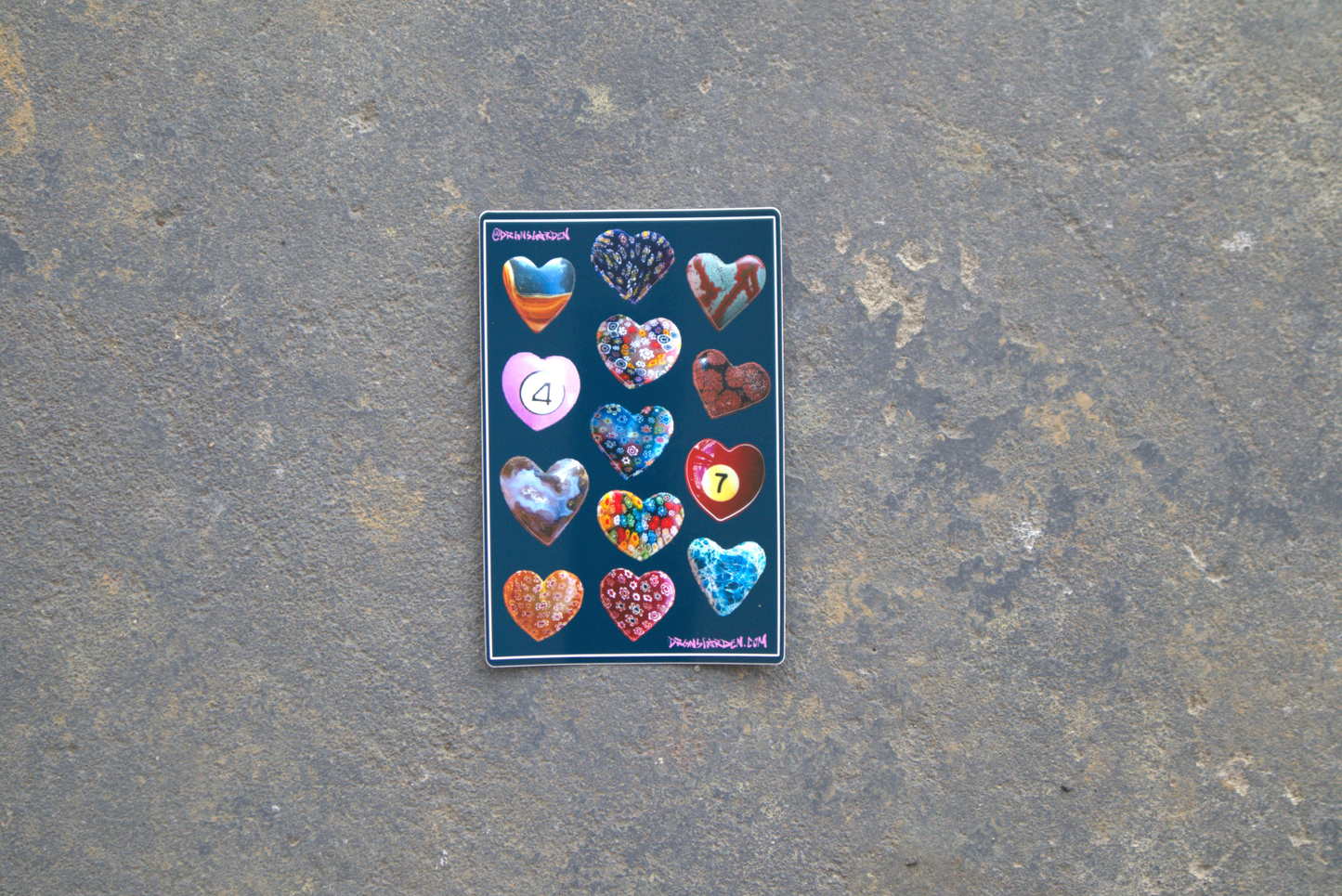 A 4" x 6" sticker sheet of 13 different heart-shaped pendant photos made into stickers. Sticker sheet sits atop a gray surface