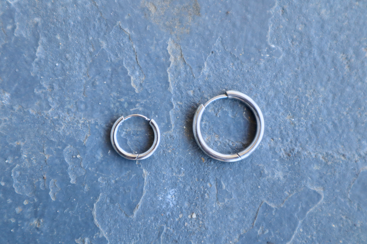 A large and small steel hoop earring resting against a blue surface