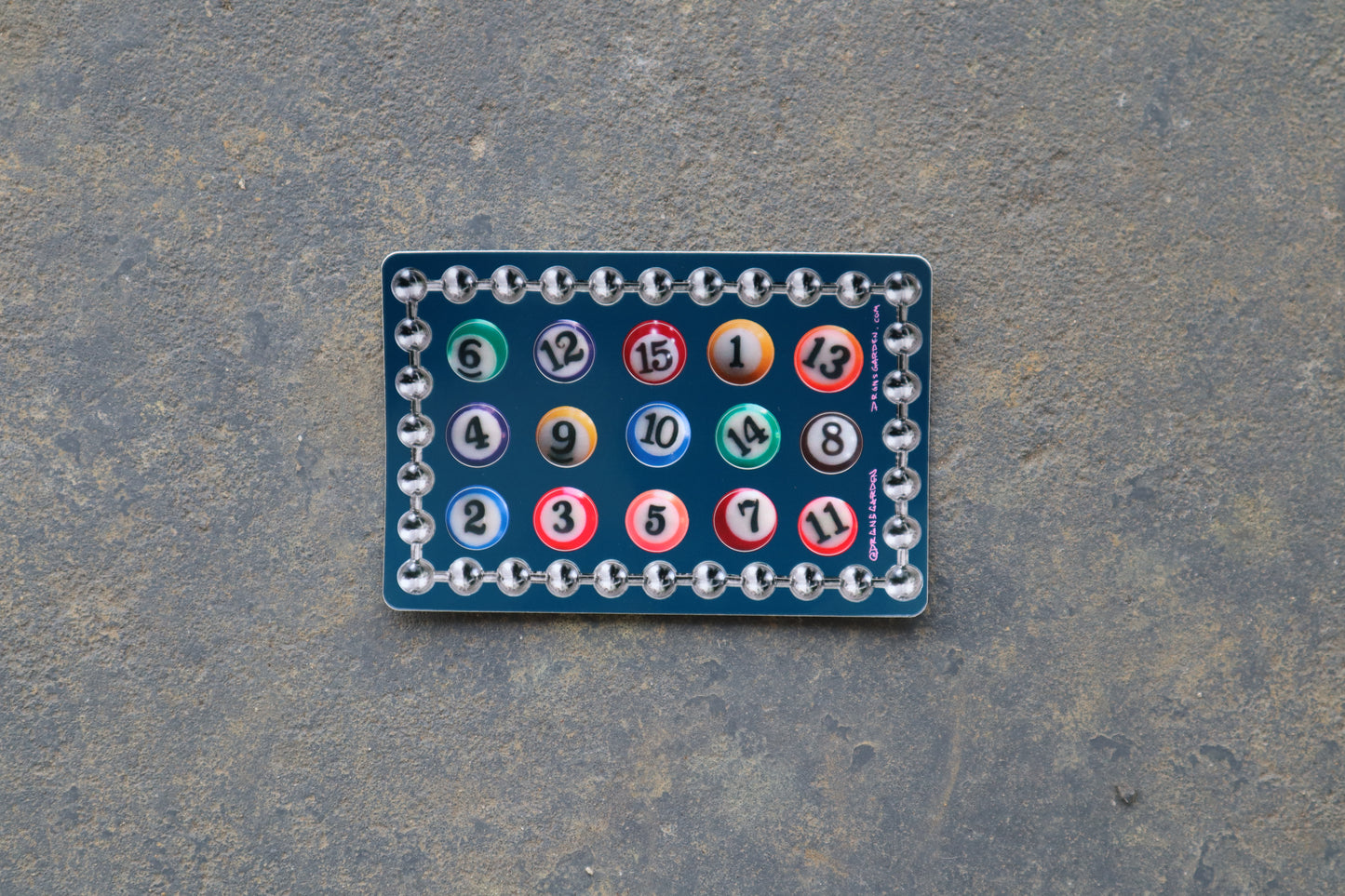 A single 6" x 4" sticker sheet with 15 different billiard ball stickers. A silver ball chain sticker lines the border of the sticker sheet. Sticker sheet sits atop a gray surface