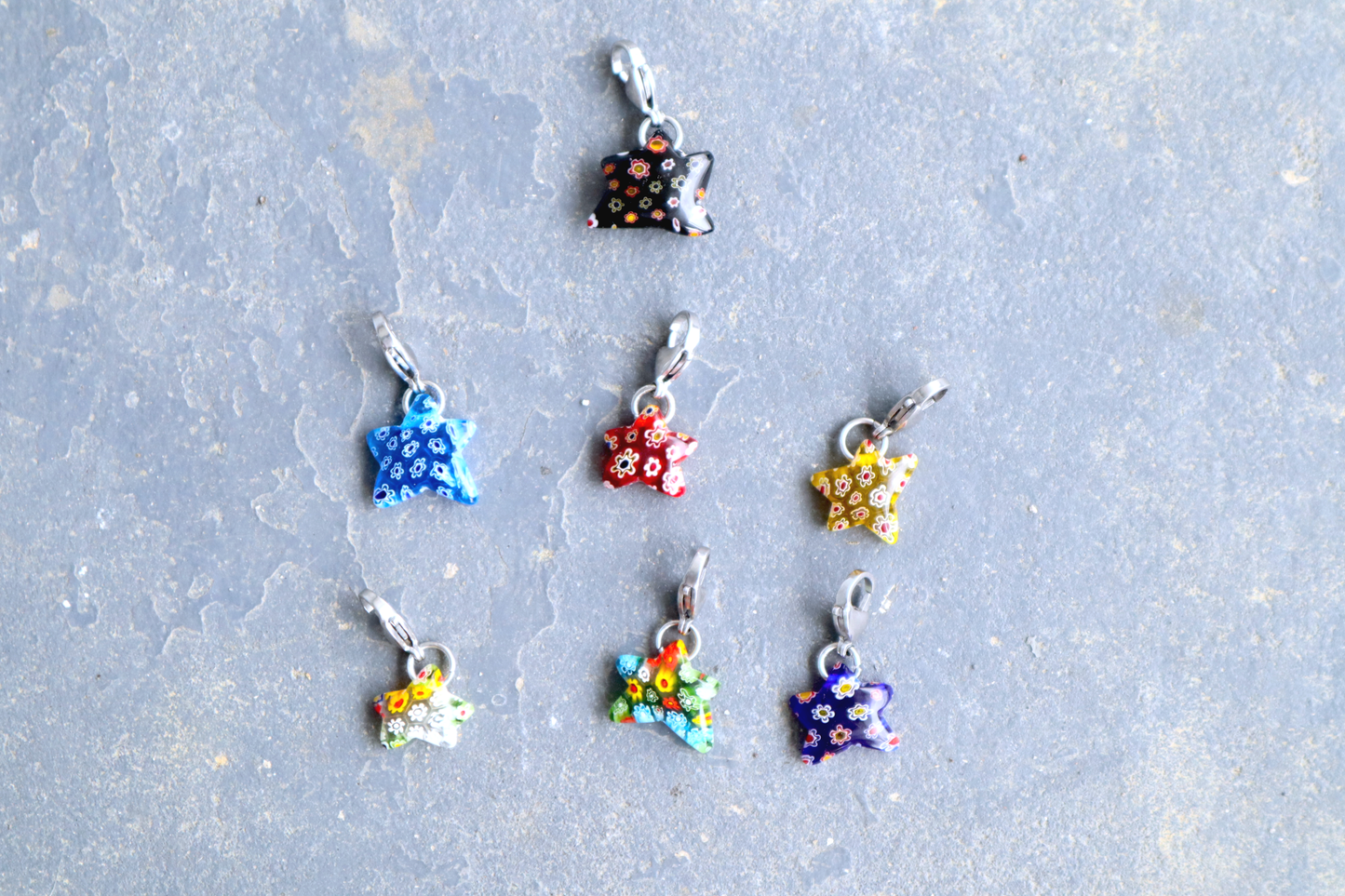 7 Star-shaped pendants with multicolored flower patterns. A silver clasp is attached to each pendant, resting on a gray surface.