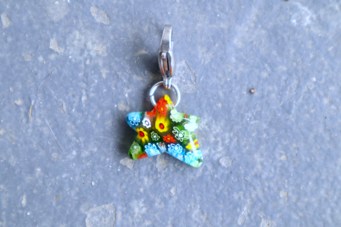 Star-shaped Multi-colored pendant with Multicolored flower patterns. A silver clasp is attached to the top of the pendant, resting on a gray surface.