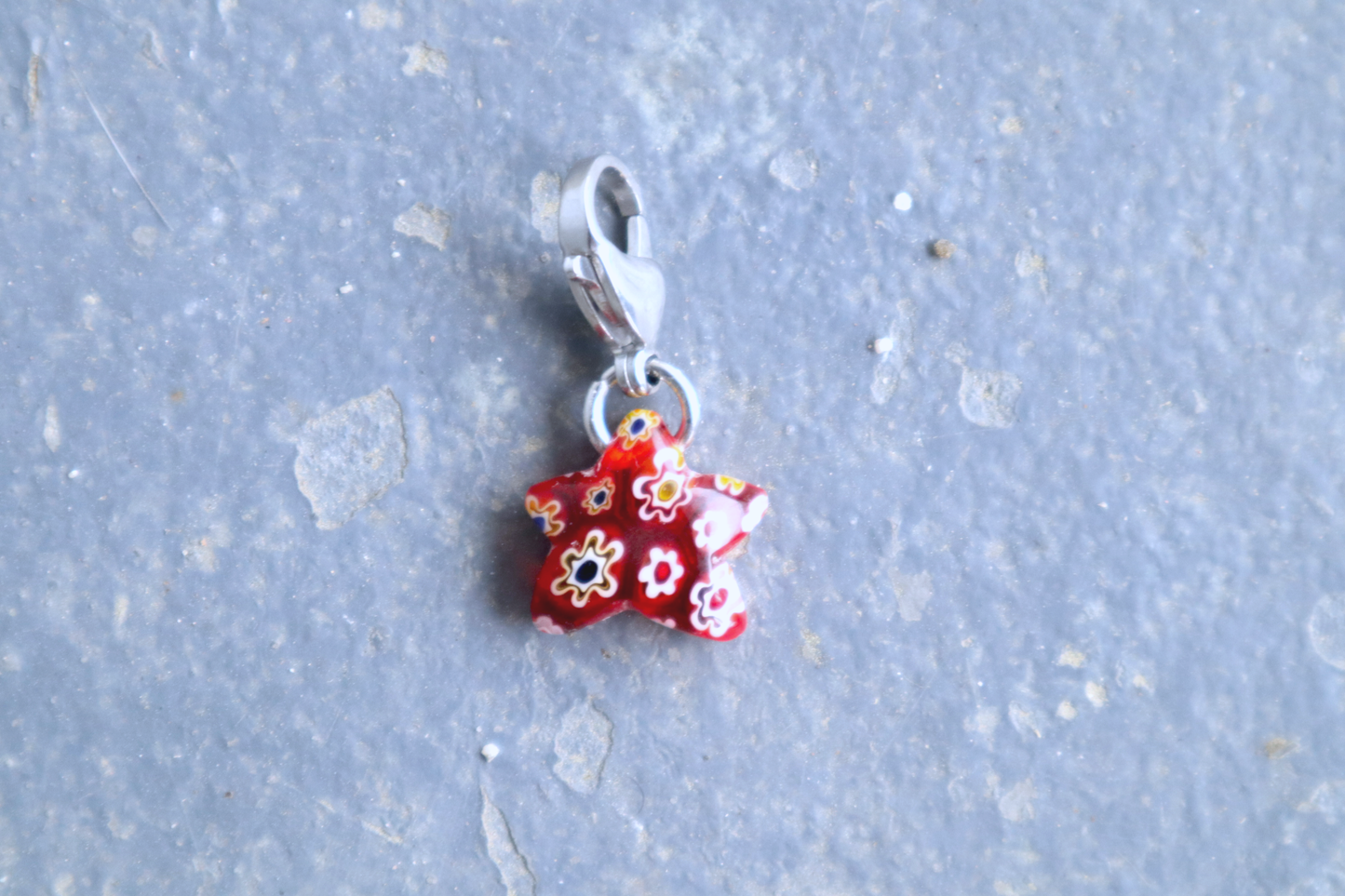 Star-shaped red pendant with white, yellow, red and blue flower patterns. A silver clasp is attached to the top of the pendant, resting on a gray surface.