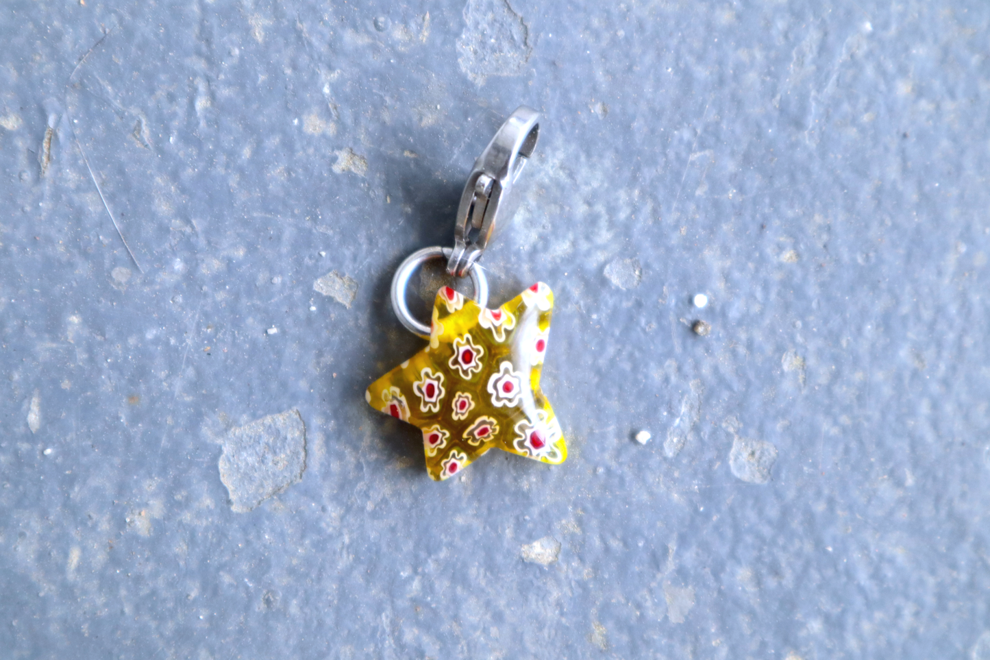 Star-shaped yellow pendant with white and red flower patterns. A silver clasp is attached to the top of the pendant, resting on a gray surface.