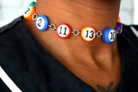 A choker made of 15 mini pool ball charms being worn on a neck. The choker has a steel chain and hardware to connect the charms.
