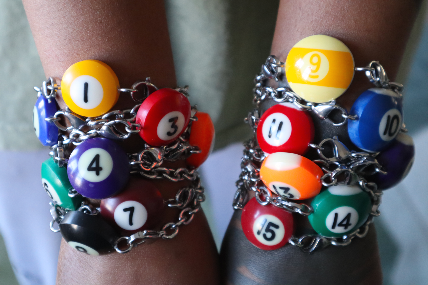 Several silver chain bracelets with billiard ball pendants worn stacked against each other on two arms.