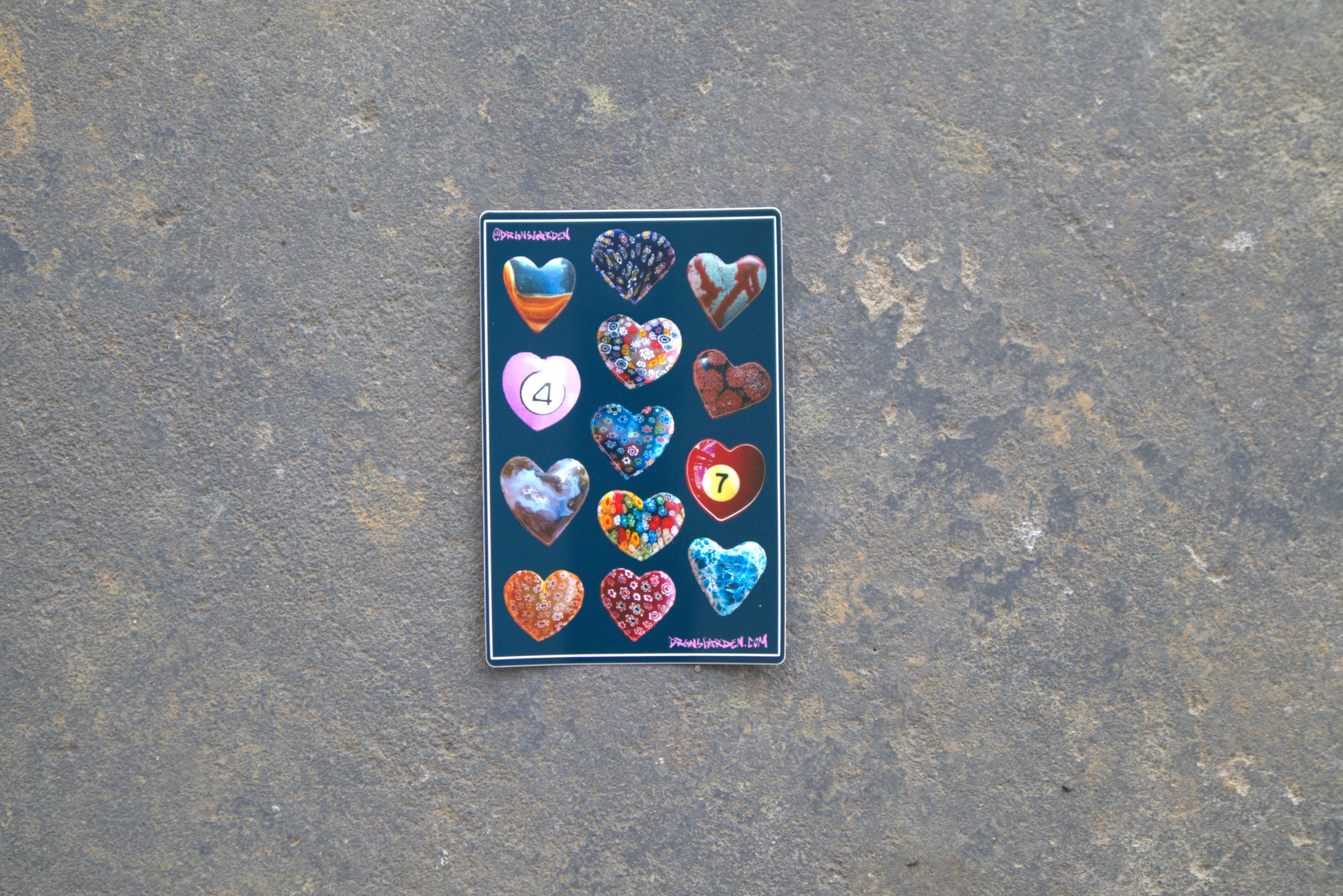 A 4" x 6" sticker sheet of 13 different heart-shaped pendant photos made into stickers. Sticker sheet sits atop a gray surface