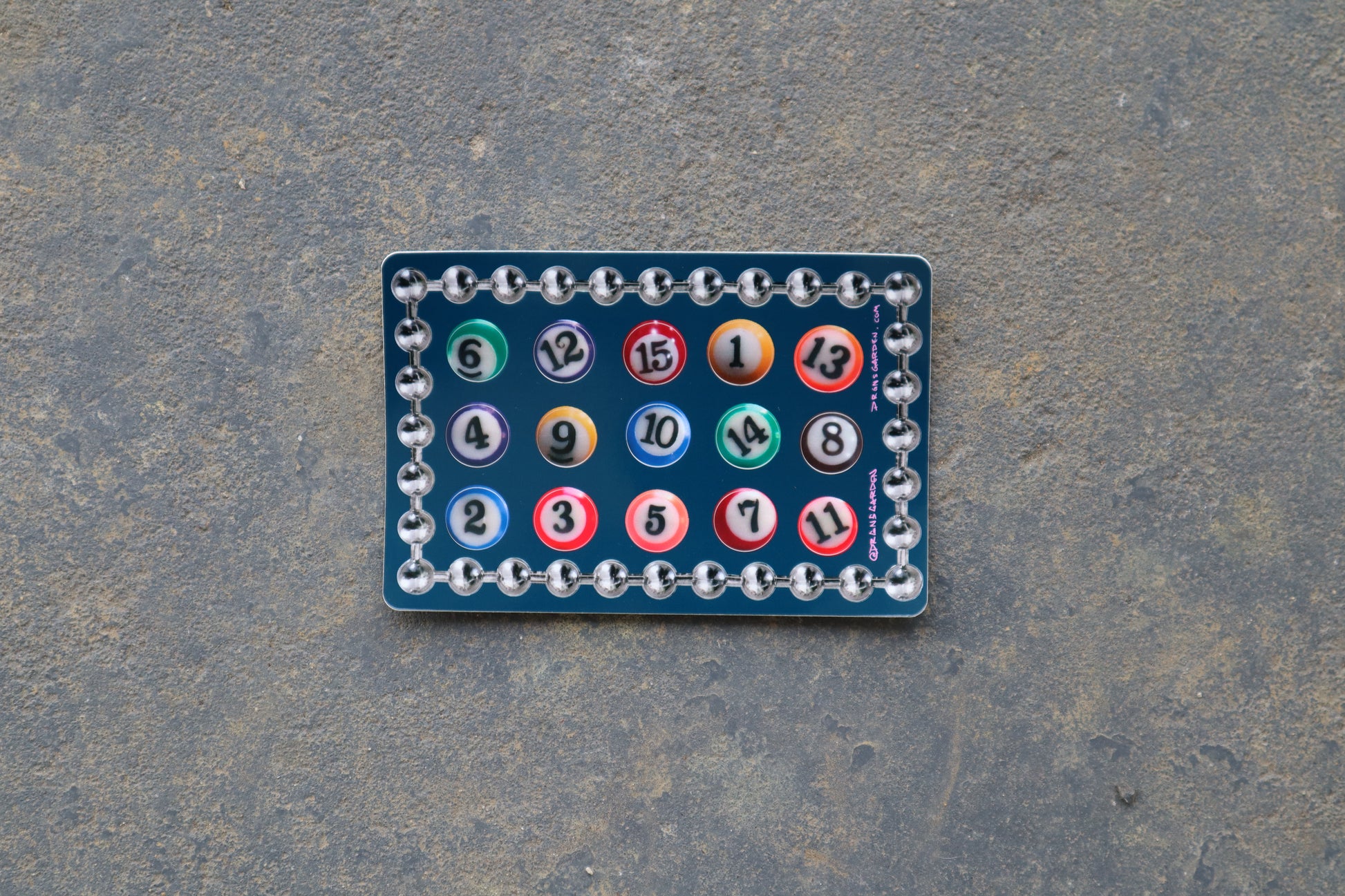 A single 6" x 4" sticker sheet with 15 different billiard ball stickers. A silver ball chain sticker lines the border of the sticker sheet. Sticker sheet sits atop a gray surface