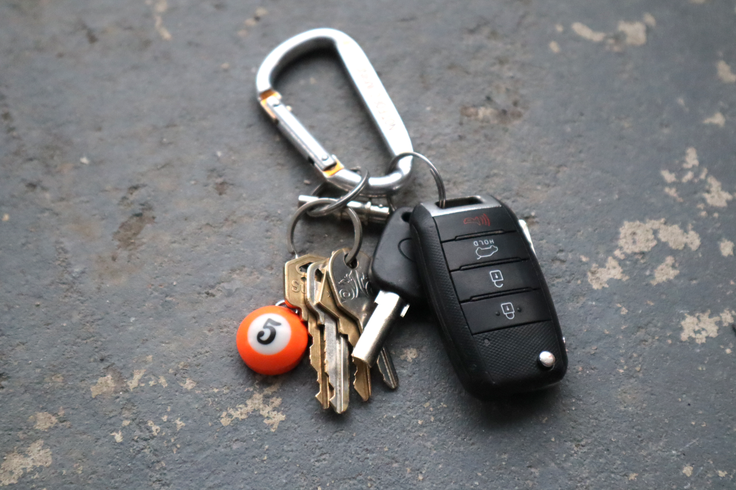 Keychain with car key, house keys, and small orange pool ball on a textured surface