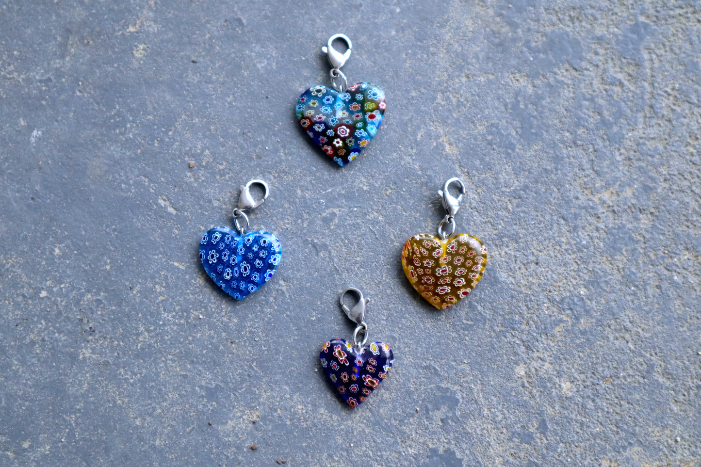 4 heart-shaped pendants with multicolored flower patterns. A silver clasp is attached to each pendant, resting on a gray surface.