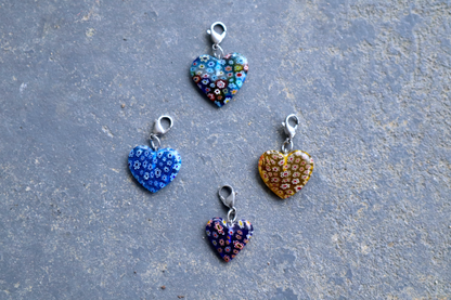 4 heart-shaped pendants with multicolored flower patterns. A silver clasp is attached to each pendant, resting on a gray surface.