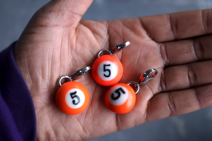 Three orange number 5 billiard ball charms on a hand.
