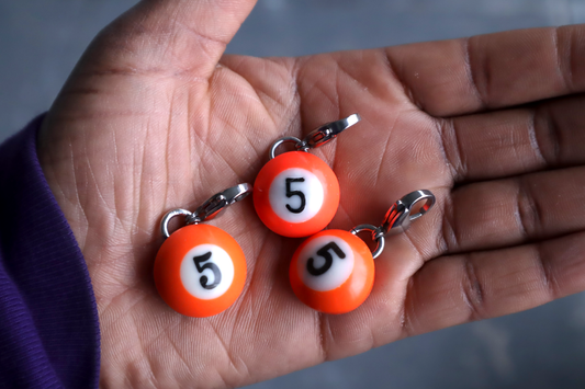Three orange number 5 billiard ball charms on a hand.