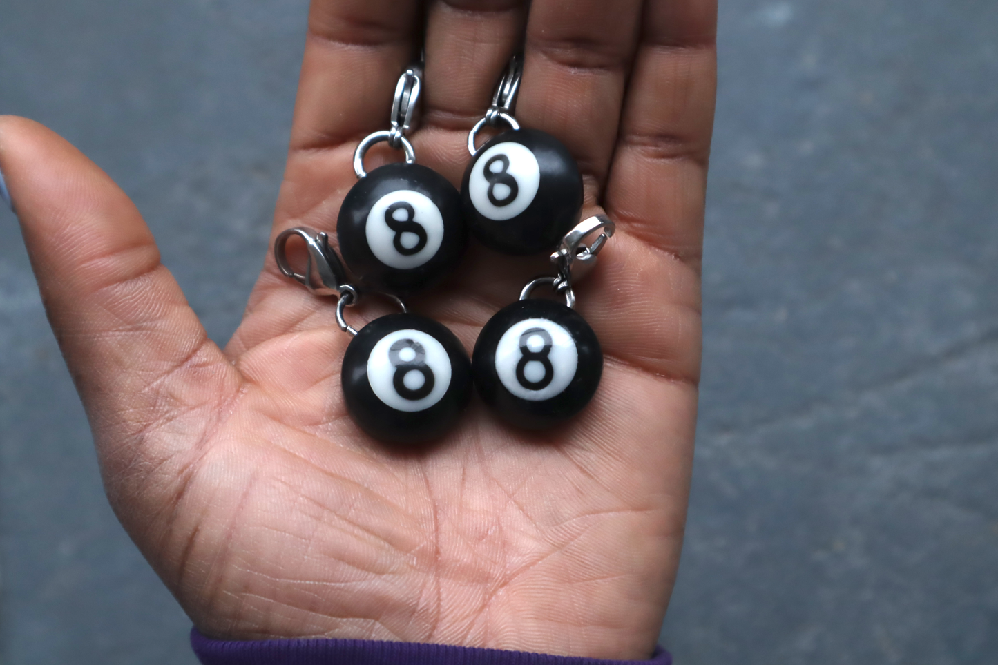 Four billiard ball keychains with number 8 on a hand against a gray background
